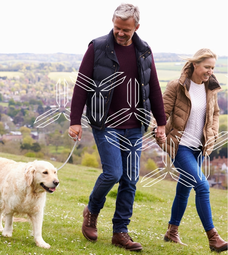 Man and woman wearing fall clothing walk golden retriever with mountains in background
