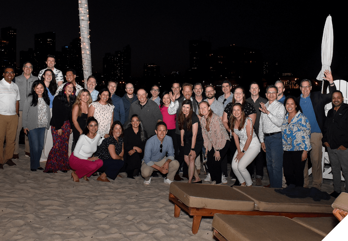 A group of people smiling and posing on the beach at night.