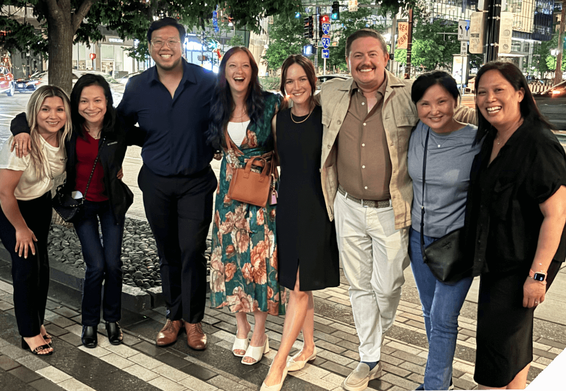 A group of people smiling and posing for a photo outside on a brick street.